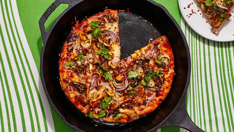 Barbecue mushroom pizza in a cast iron skillet on a green striped tablecloth.