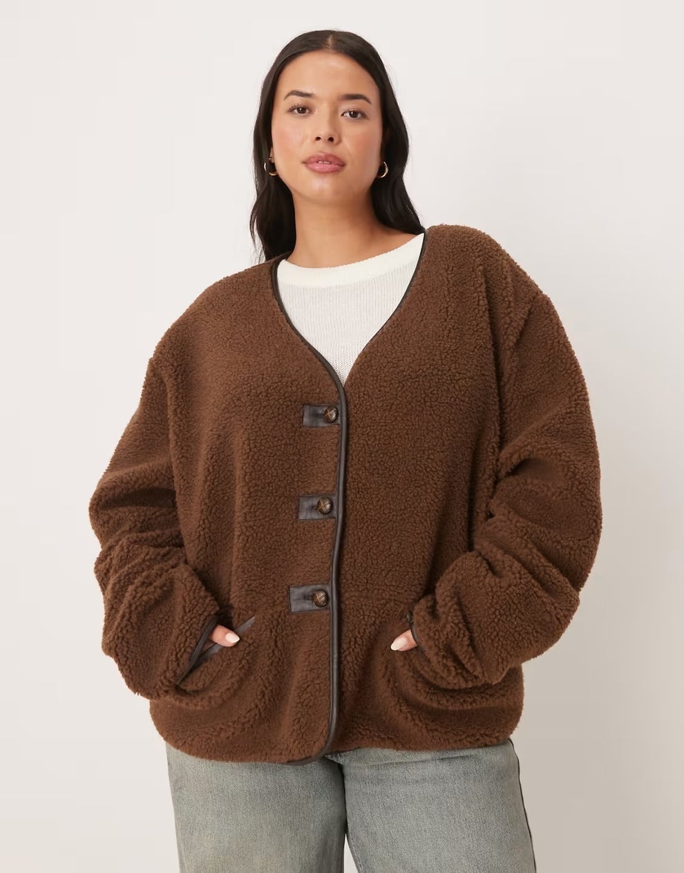 Person wearing a cozy, textured cardigan with a white top underneath, and jeans. Hands in cardigan pockets