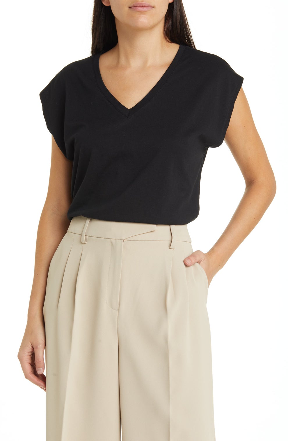 Person wearing a V-neck short-sleeve top and high-waisted pleated trousers, standing with one hand in a pocket