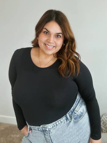 reviewer smiling, wearing a long-sleeve black top tucked into high-waisted jeans