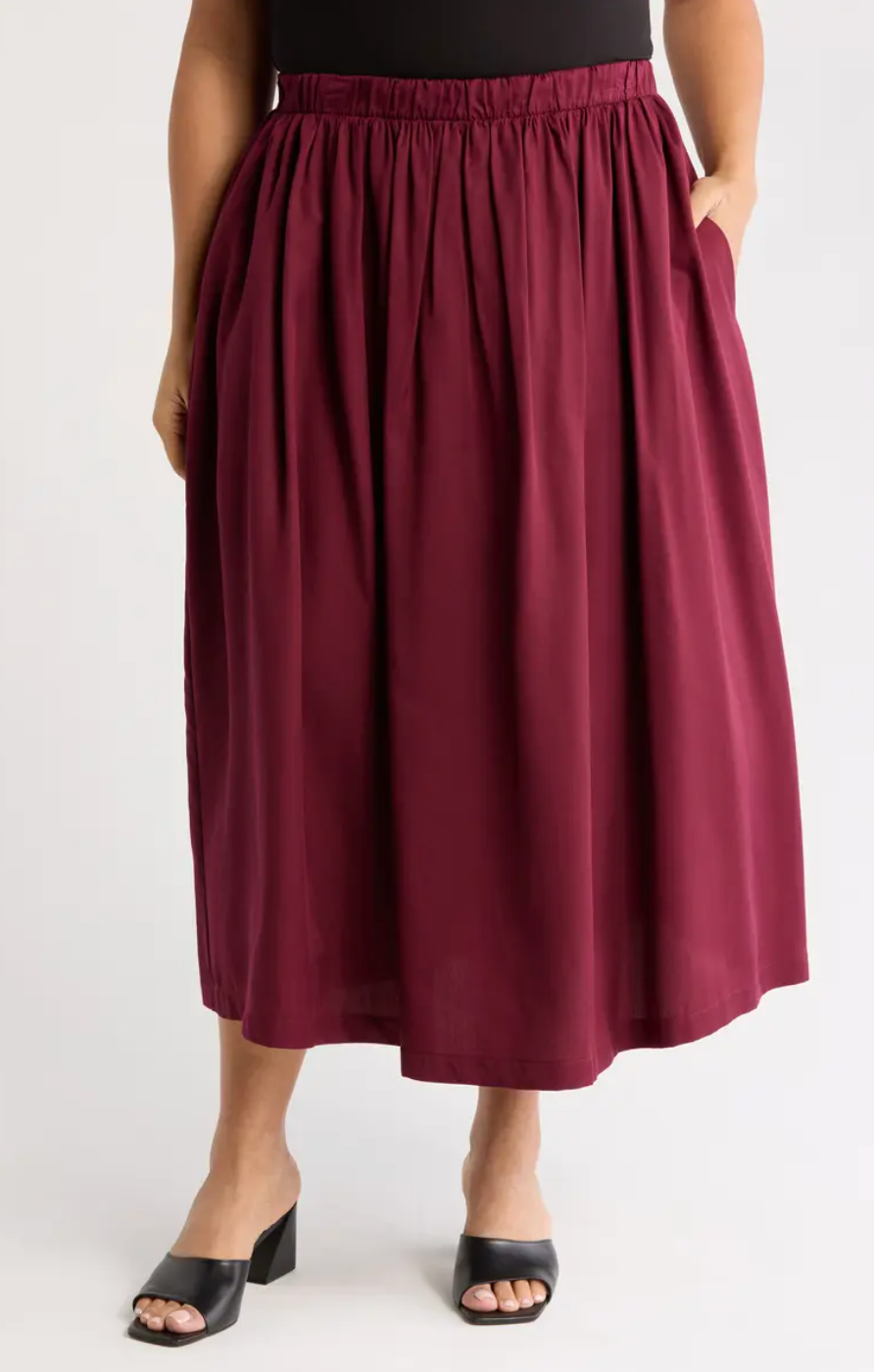 A person wearing a pleated midi skirt with an elastic waistband and pockets, paired with open-toe block heels