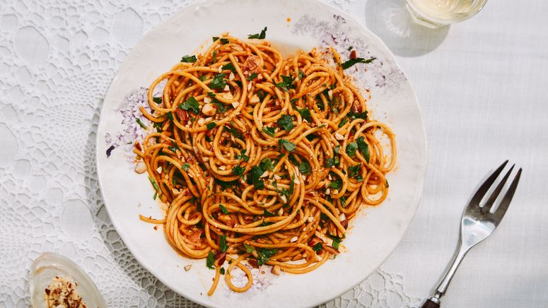 A white plate of winding spaghetti topped with chopped cilantro and nuts all against a white lace table setting.