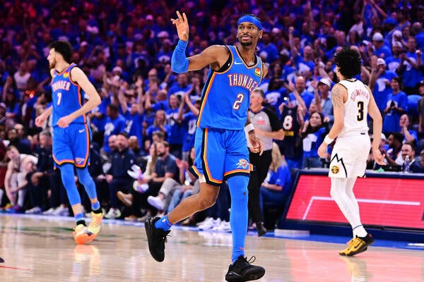 Shai Gilgeous-Alexander, in an Oklahoma City Thunder uniform and black sneakers, holds one hand in the air while running on the court.
