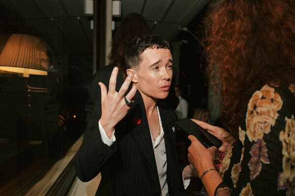 A young man with an intense expression gestures with his right hand.