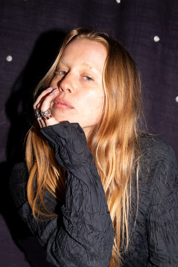 A portrait of Sylvie Macmillan, who has dirty blond hair and one hand propping up her chin. She is wearing a black crinkled shirt.