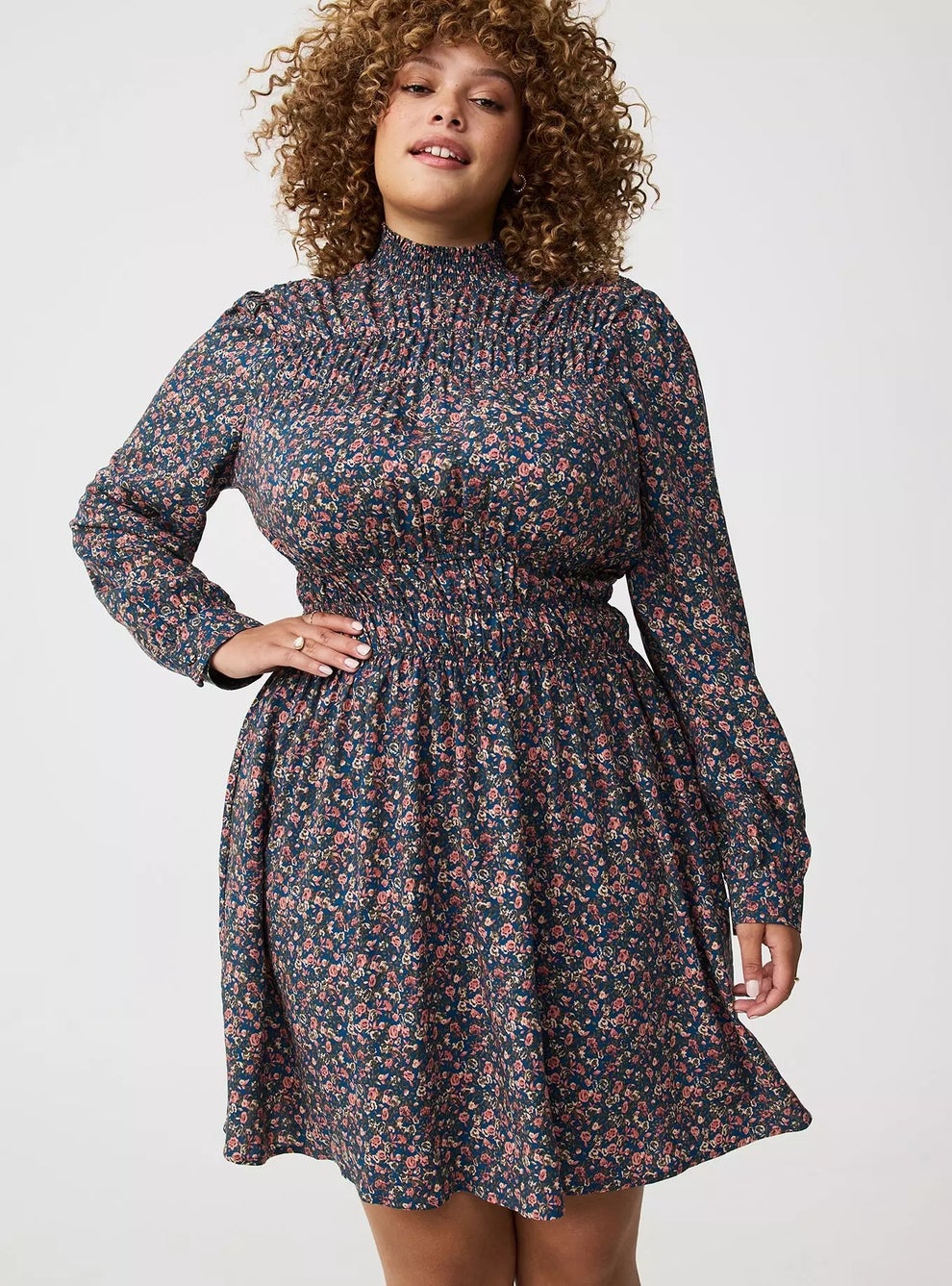 Person wearing a floral-patterned, long-sleeve, high-neck dress with a smocked waist, suitable for a casual or semi-formal setting