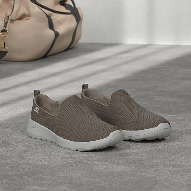 Slip-on casual sneakers with textured uppers on a concrete floor, next to a beige bag