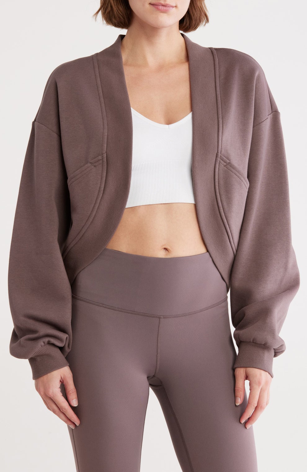 Person modeling a cozy, relaxed-fit jacket over a white crop top and leggings, showcasing casual athleisure fashion