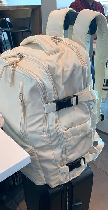 A reviewer's beige backpack on top of their suitcase