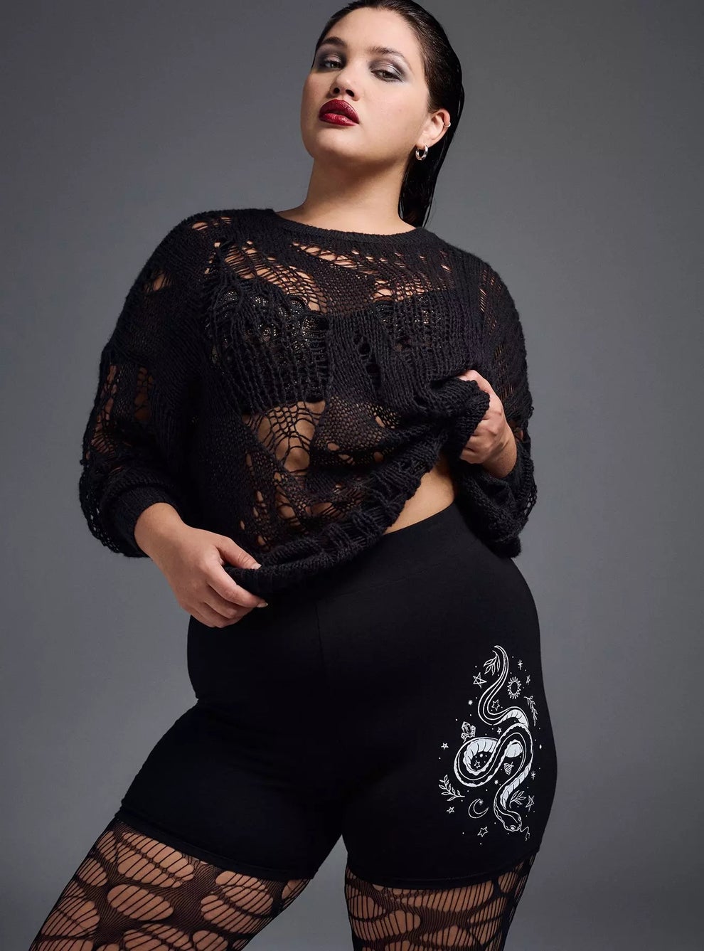 Person poses in stylish black knit outfit with mesh details and shorts featuring a snake design