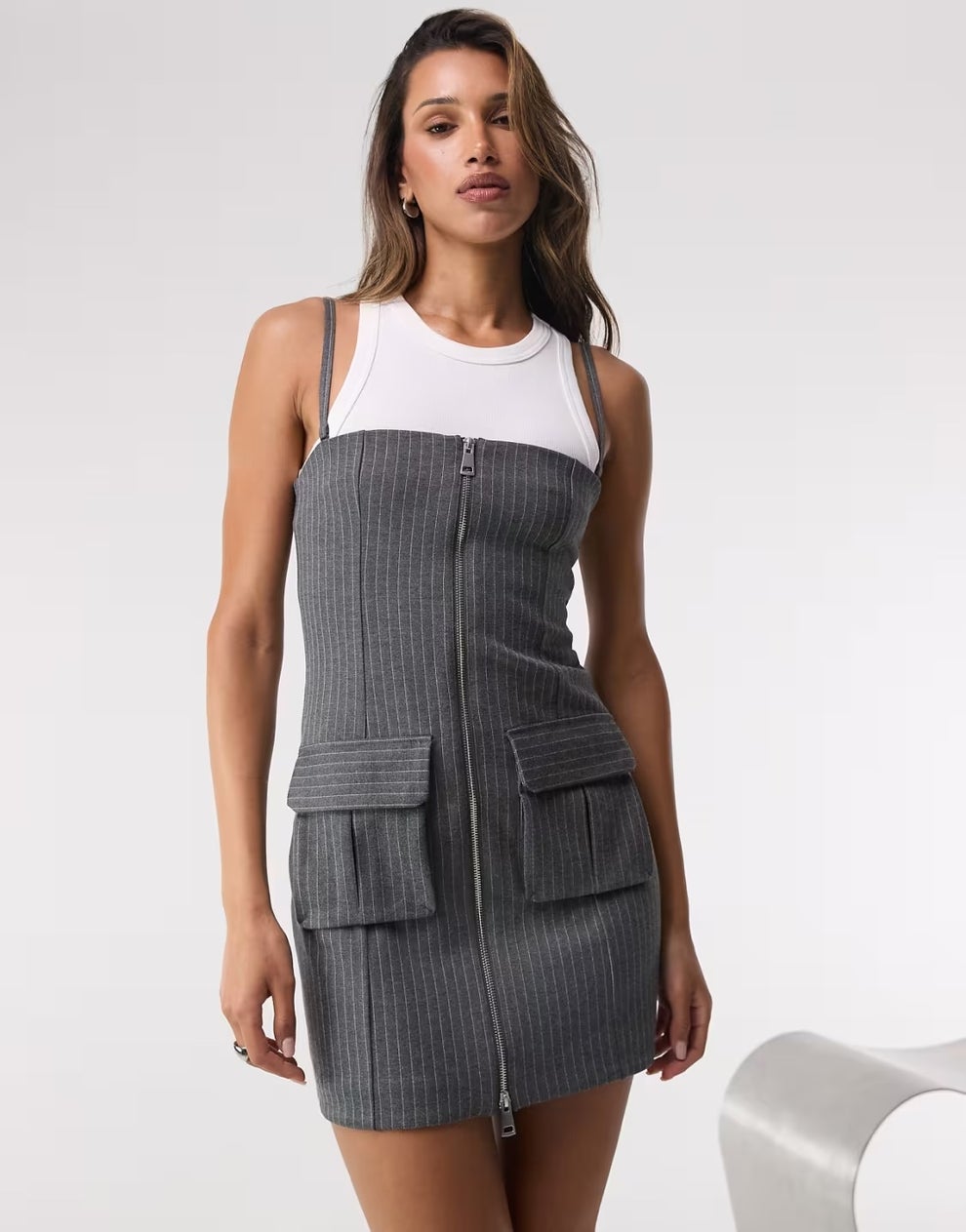 Person wearing a sleeveless pinstripe dress with front pockets and a white undershirt-style top