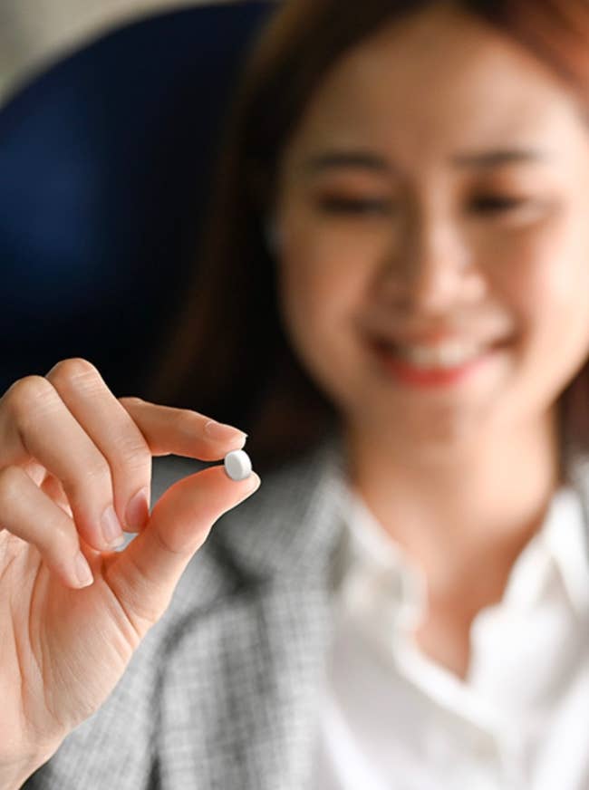 model holding a small white pill, smiling, wearing a blazer