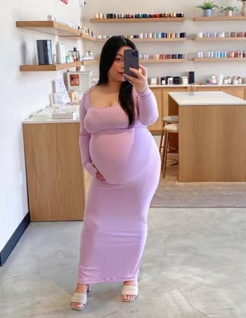 Person taking a mirror selfie in a store, wearing a long fitted dress and sandals. Shelves with various products are in the background