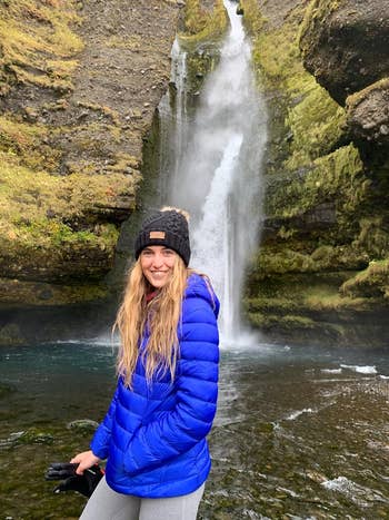 A reviewer wearing the blue puffer jacket in fron of a waterfall in Iceland