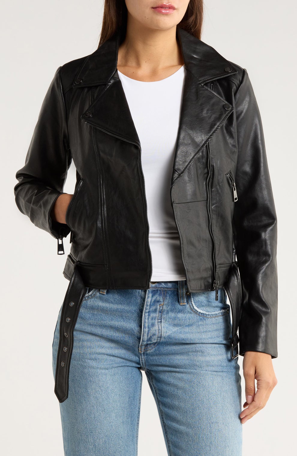 Person wearing a black leather jacket over a white shirt and blue jeans, with one hand in a pocket