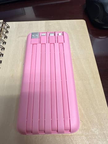 Pink portable power bank with multiple USB ports, displayed on a desk