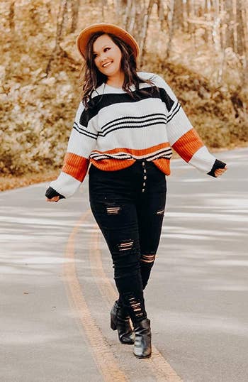 a reviewer wearing the sweater featuring white black and orange stripes 