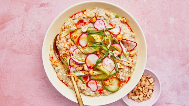 A bowl of savory oatmeal topped with shaved radishes pickled cucumbers green onions and chopped peanuts.
