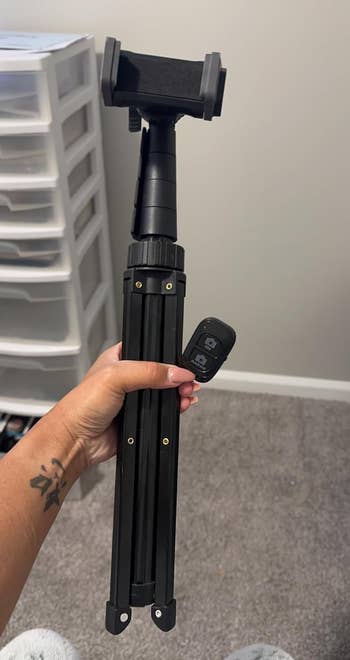 reviewer holding a compact tripod with a smartphone mount and remote control, suitable for on-the-go photography