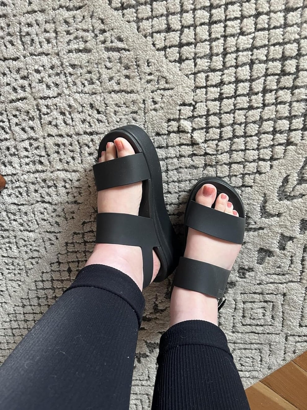 Person wearing black strappy sandals with black leggings on a textured carpet