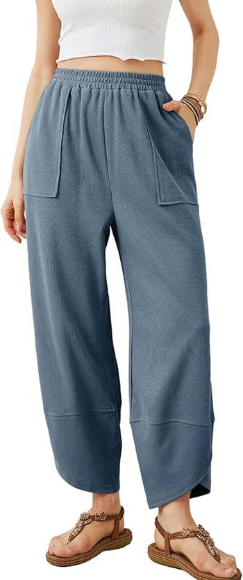 model wearing loose-fit pants with a ribbed texture and a sleeveless top, accessorized with bracelets and sandals