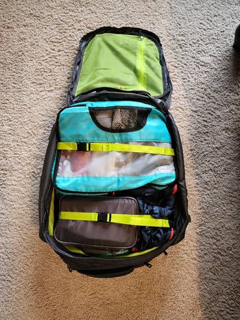 Open travel backpack with organized packing cubes and compartments on a carpeted floor. Ideal for efficient packing and organizing travel essentials