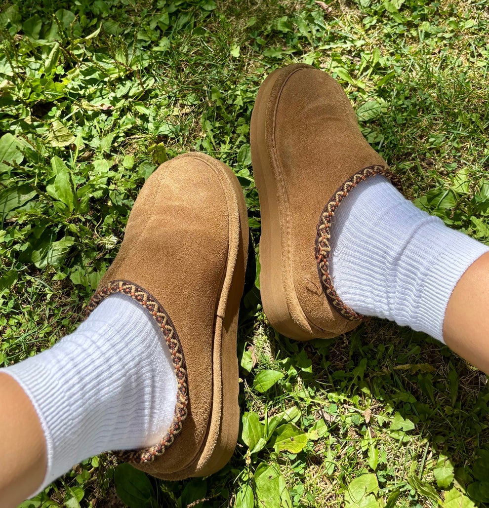 Person wearing slip-on shoes with socks, sitting on grass