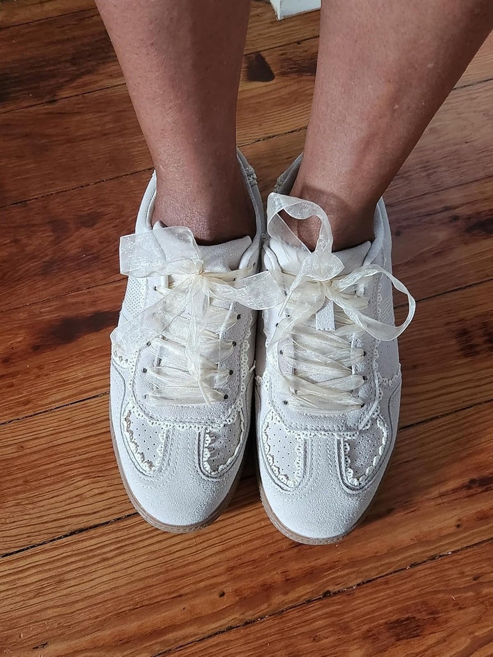 White sneakers with sheer ribbon laces on a wooden floor