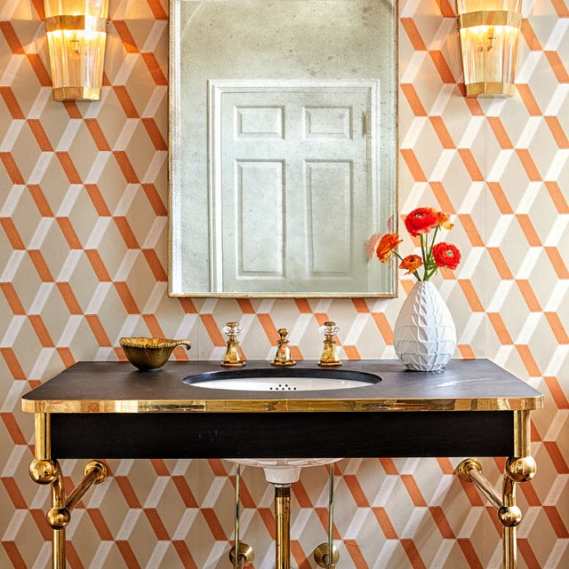 black sink with metal legs and hardware against a patterned orange and white wallpaper and art deco looking sconces on either side of a long mirror