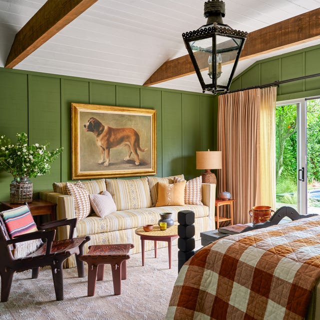 a bedroom with green paint walls with a large photo of a dog on one side and a light striped sofa with low wood tables in front and then opposite a bed with a brown and white large check blanket at the foot