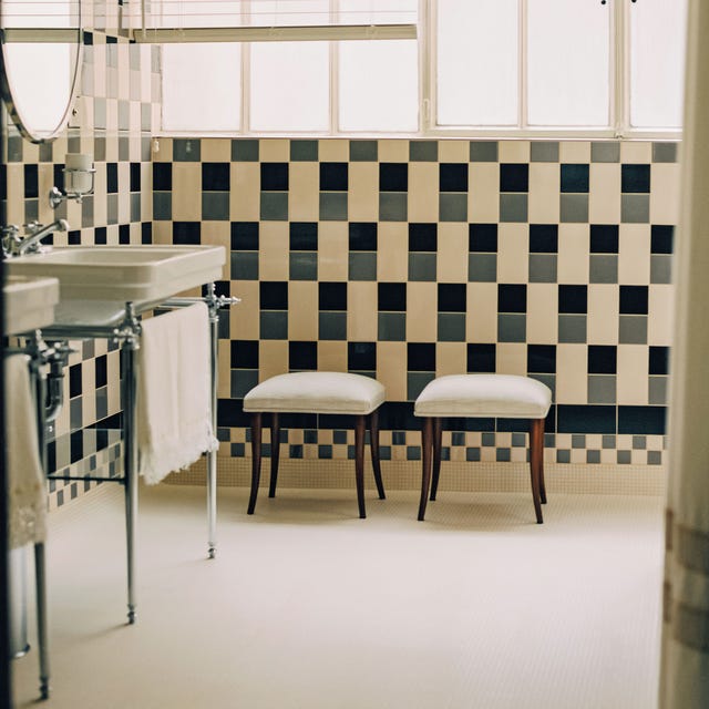 a bathroom with black and gray and cream grid tiles with a vanity on silver legs and stools