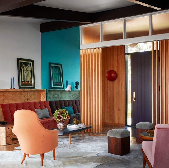 living area with built in sofa with red tufted cushioning and a low cocktail table and architectural beam details that look draperies between the area and the hall and a orangey chair and some low gray velvet pillow topped stools
