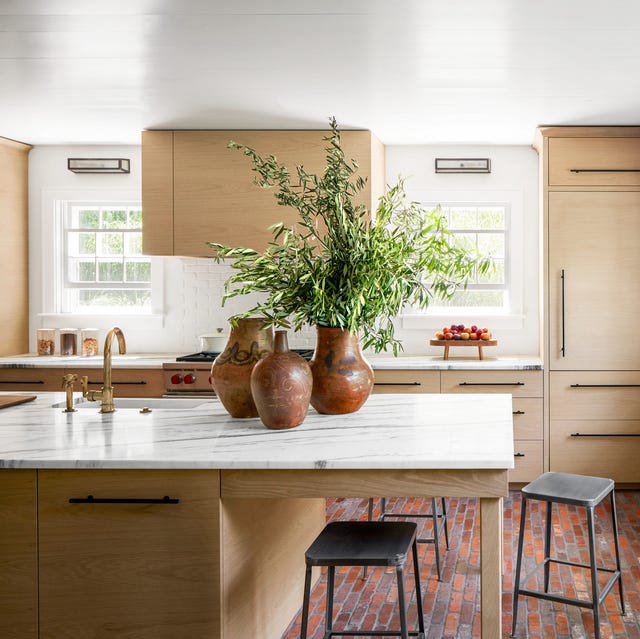 a light wood kitchen with a plant in one of three terra cotta vases on the counter and some metal stools