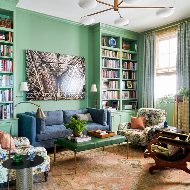 green living room with inset bookshelves on either side of a blue sofa with a photo above it and a patterened rug and several mismatched armchairs