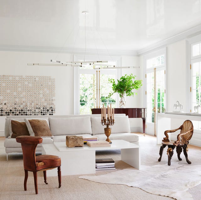a very white airy living room with a white sofa and a table and unusual dark stained armchairs