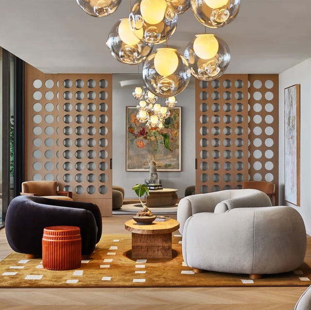 a living room with a lattice screen behind and large bean bag like armchairs on a caramel colored rug with white squares and a bubble chandelier