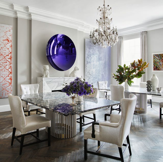 a very white dining room with a chandelier and a table with chairs and a large oval purple artwork over the fireplace mantel