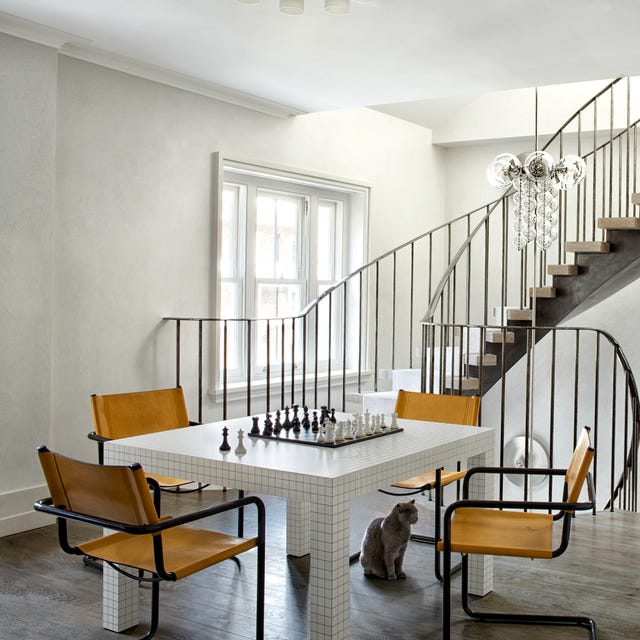 a white blocky game table with yellow chairs on an open landing with swoopy staircases going up and down