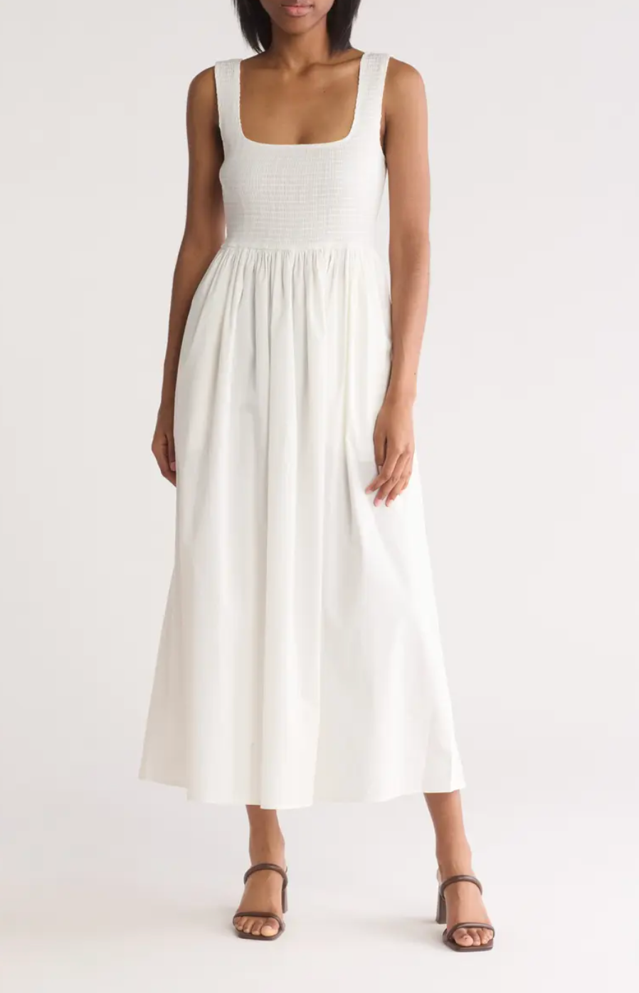 Person in a sleeveless, square-neck, long dress with a fitted bodice and flowing skirt, wearing strappy sandals
