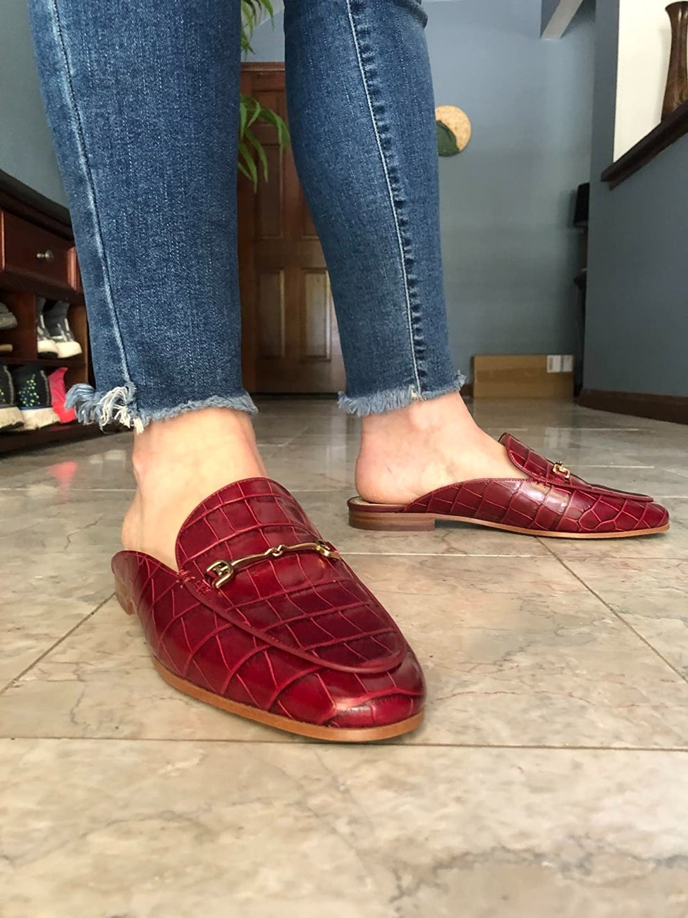 Person wearing red textured slip-on loafers and frayed-hem jeans indoors, showcasing footwear fashion