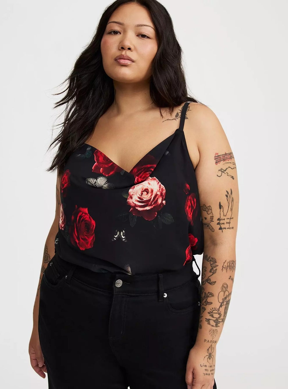 Person in floral-patterned camisole with tattoos on arms, wearing dark jeans