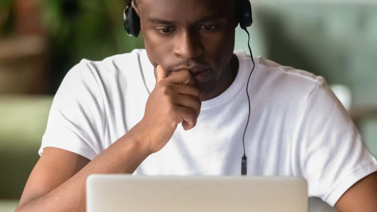 A man studies the screen of his laptop intently while wearing headphones