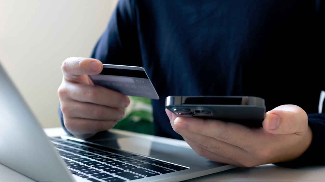 Man holding credit card, phone, laptop.