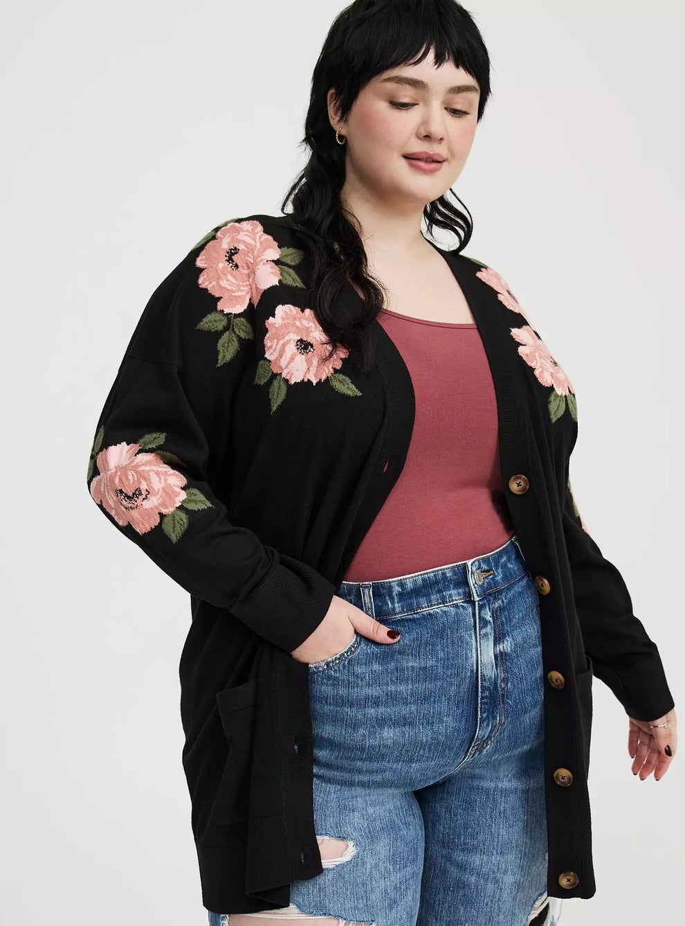 Woman wearing a floral-embroidered cardigan over a tank top and jeans, posing confidently