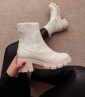 reviewer wearing one of the beige boots and holding the other