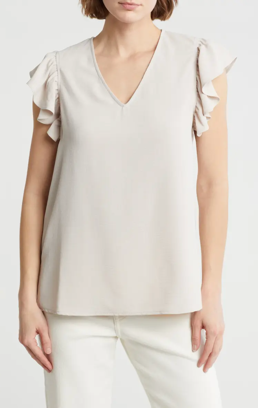 person models a sleeveless V-neck top with ruffled shoulders, paired with light pants