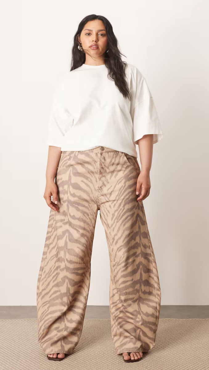 Person wearing a loose white T-shirt and wide-leg, tiger-patterned pants, standing on a neutral background