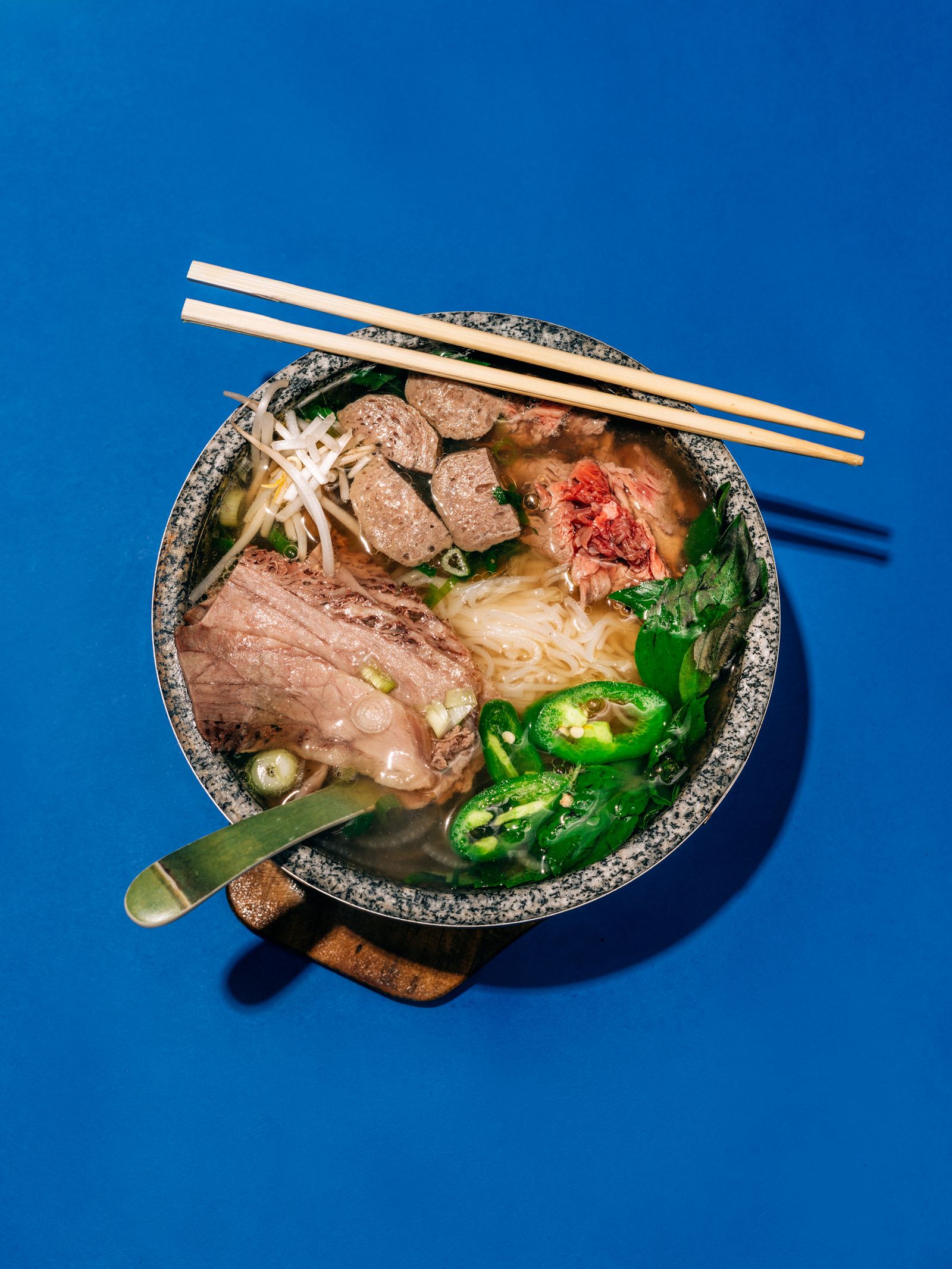 A bowl of Pho in a hot bowl on a blue background