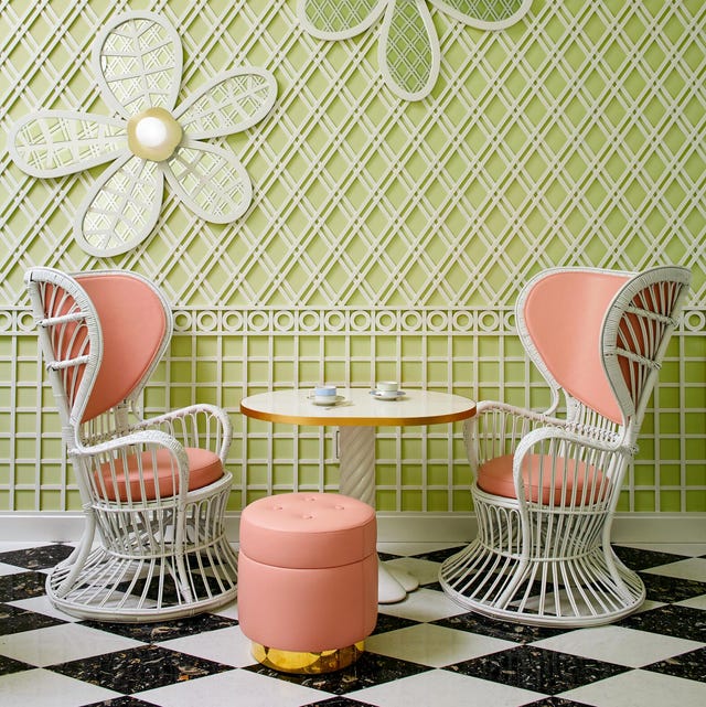 garden room with light green walls with lattice overlaid on it with daisy designs and a small white pedestal table flanked by two modern white garden wicker chairs with peachy colored cushion backs and seats and a small round stool in the same fabric with a gold base
