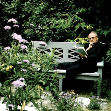 a person sitting on a bench reading a newspaper surrounded by flowers and bushes